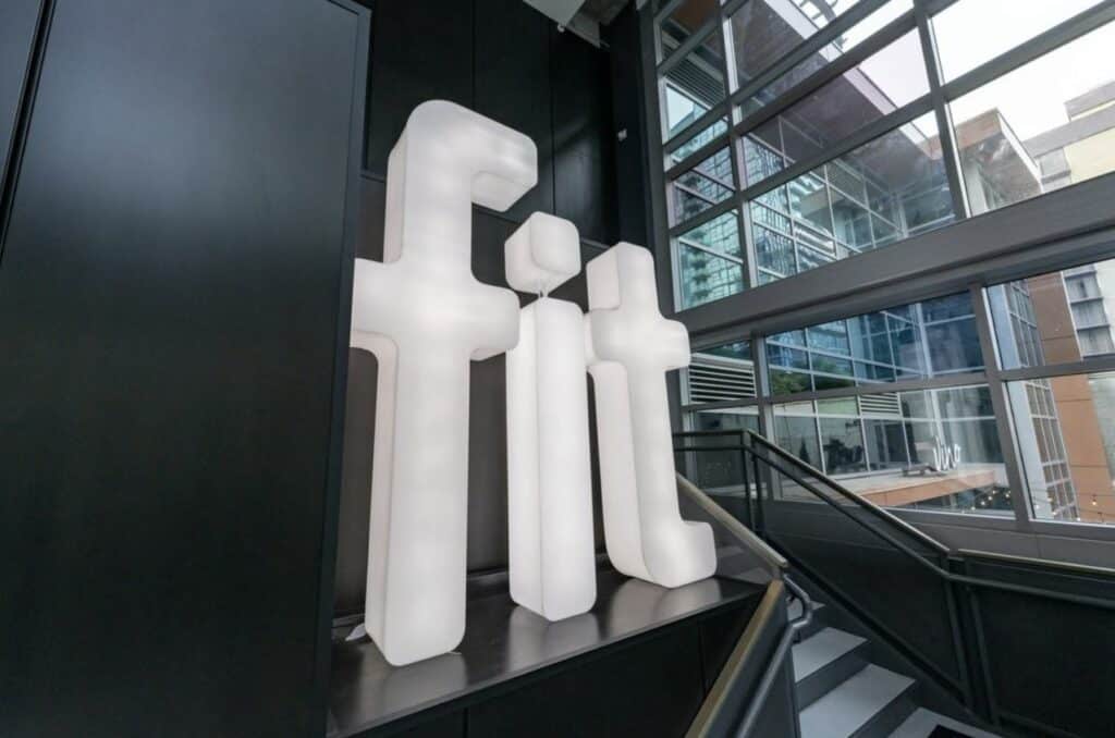 A large white sculpture with the word fit on it in front of a building.
