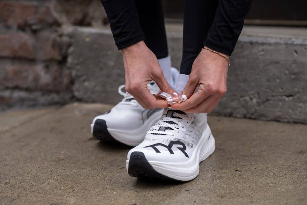 Person tying white athletic shoe with black logo on a concrete surface.